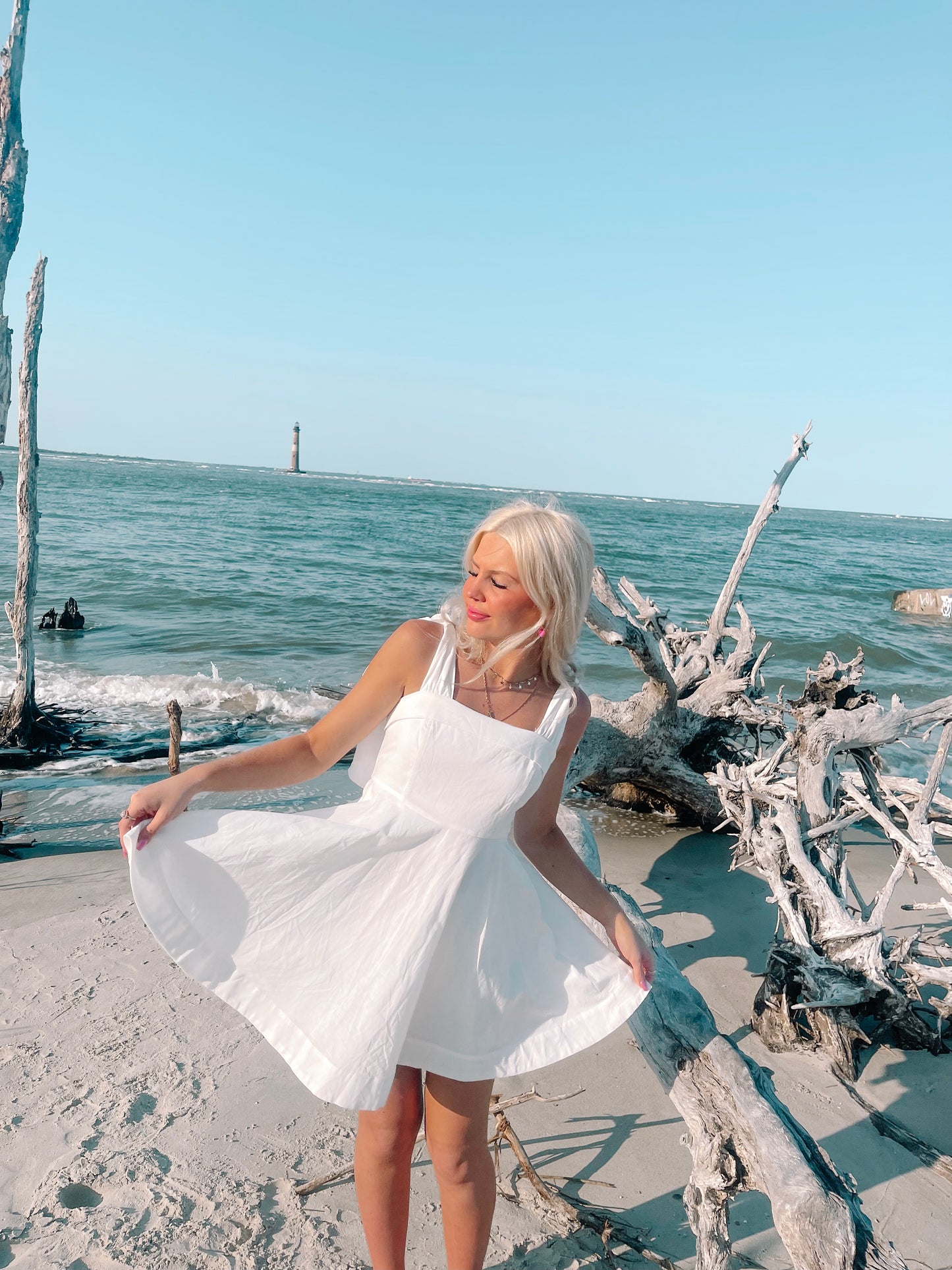 White sundress on beach; girl twirling near driftwood, ocean view.