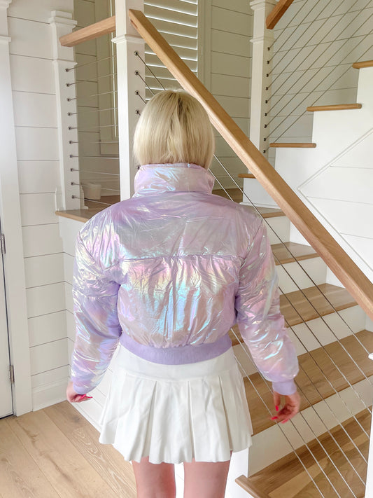 Iridescent lilac puffer jacket shown from the back, in a bright home interior.