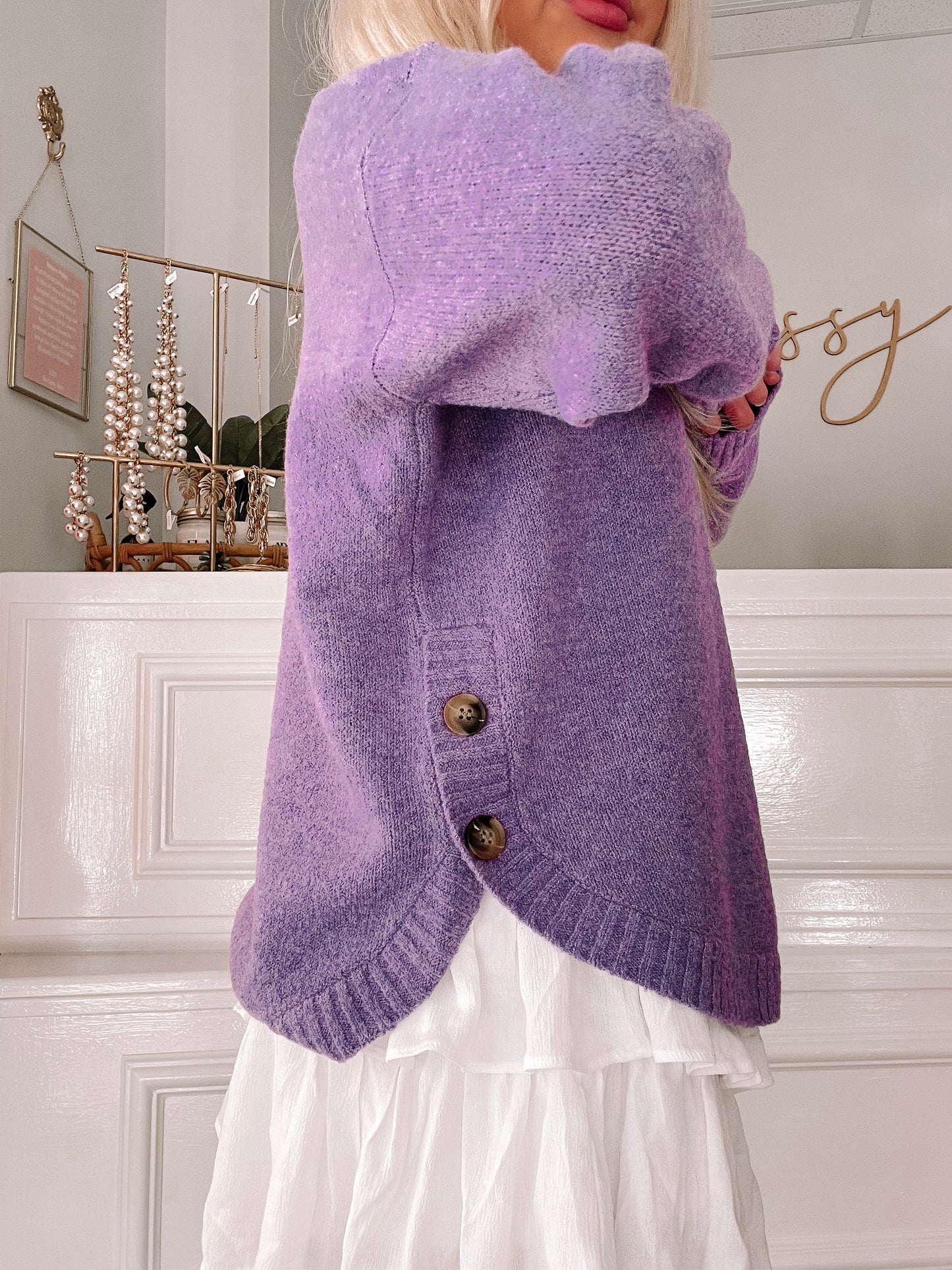 Purple knit sweater with button details, shown styled with a white tiered skirt.