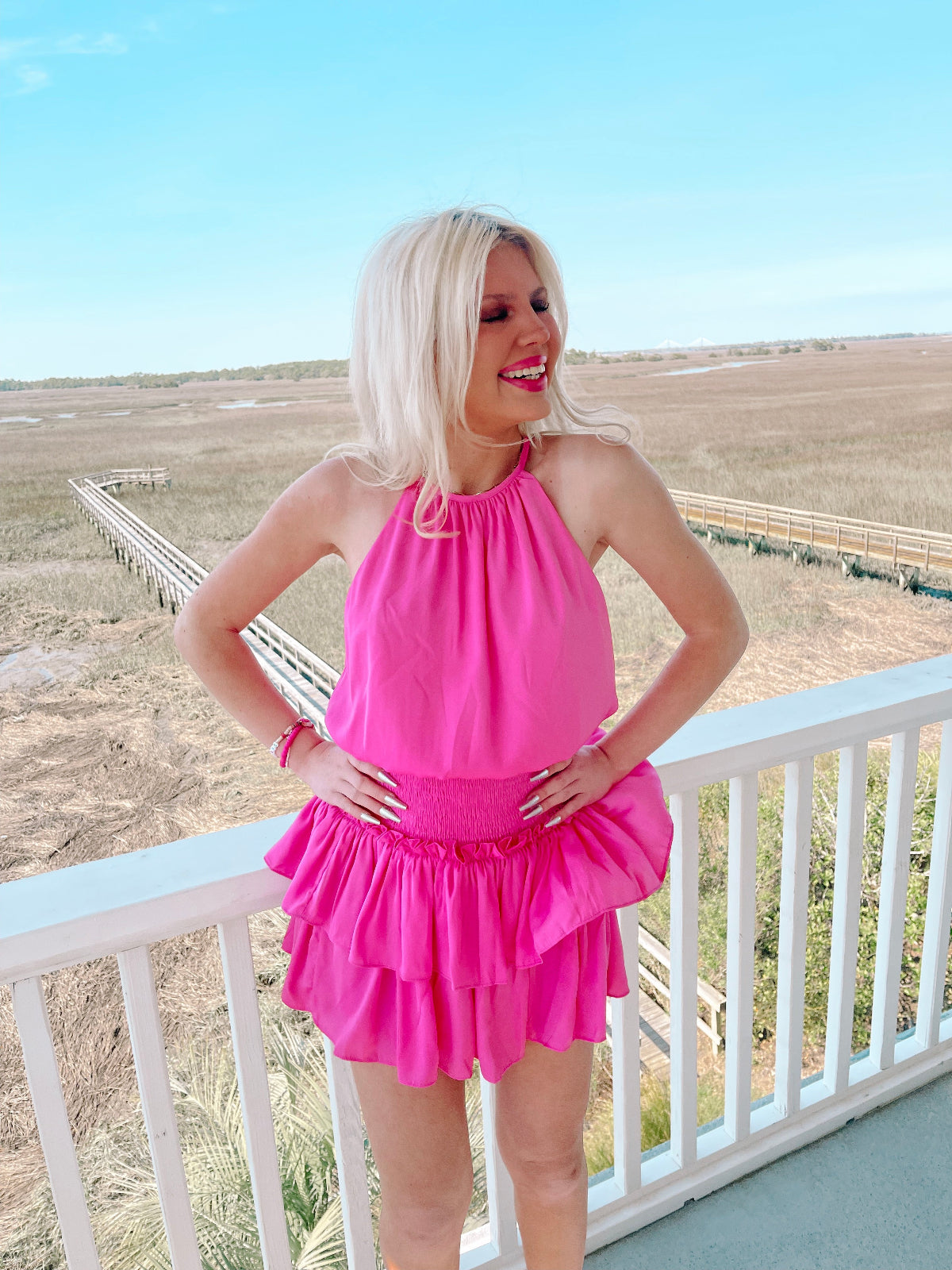 Hot pink tiered mini dress worn outdoors on a deck overlooking marshland.