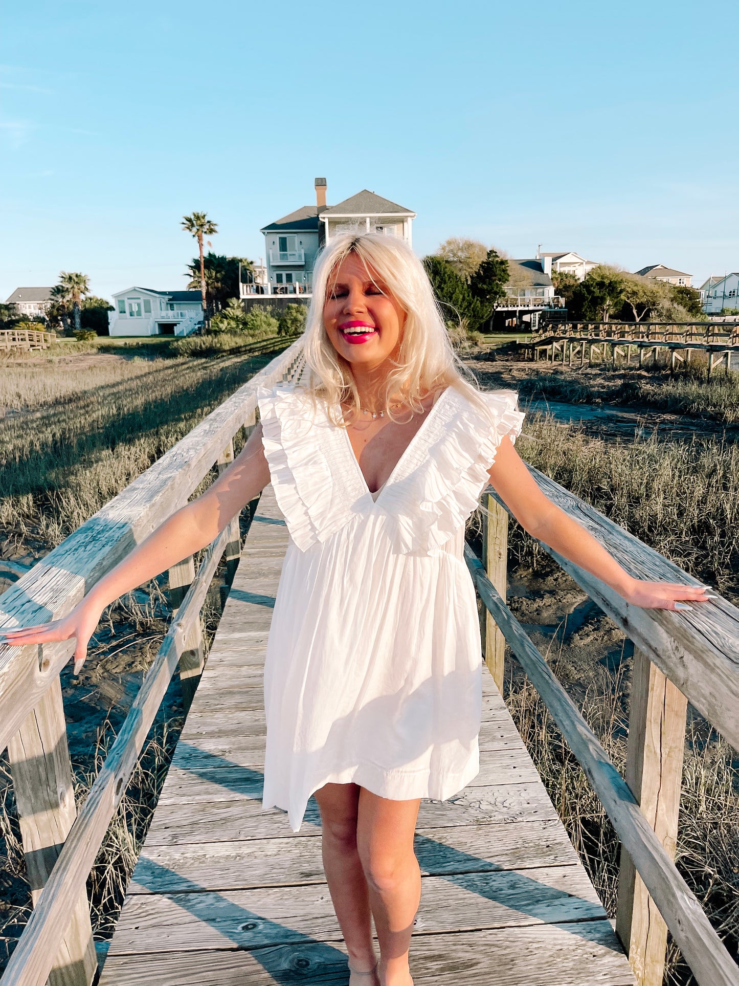 White eyelet mini dress on a wooden boardwalk, sunny coastal background.