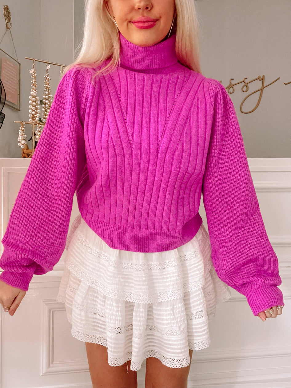 Fuchsia pink ribbed knit turtleneck sweater with balloon sleeves, styled with a white eyelet mini skirt.