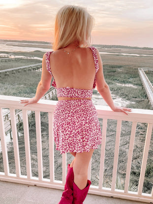 Floral print mini dress and pink boots viewed from behind, overlooking a tranquil marsh at sunset from sassy shortcake