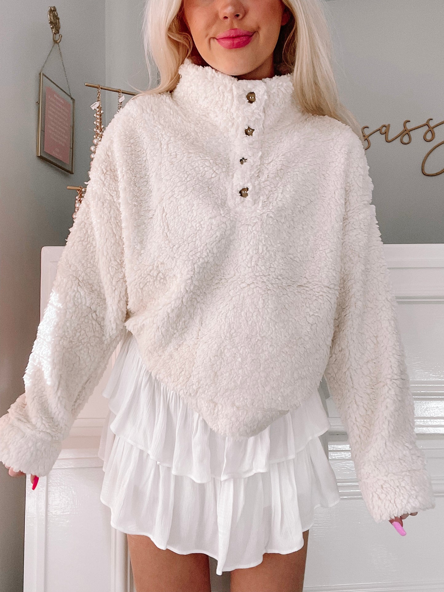 Cream-colored sherpa pullover with button details, modeled with a white ruffled skirt.
