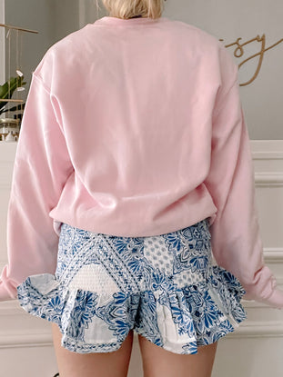 Blue and white paisley print shorts with a ruffled hem, worn with a pink sweatshirt.