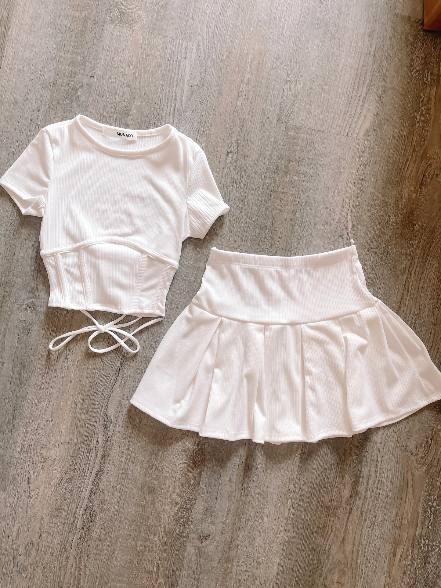 White ribbed knit crop top and pleated mini skirt set, laid flat on wood.