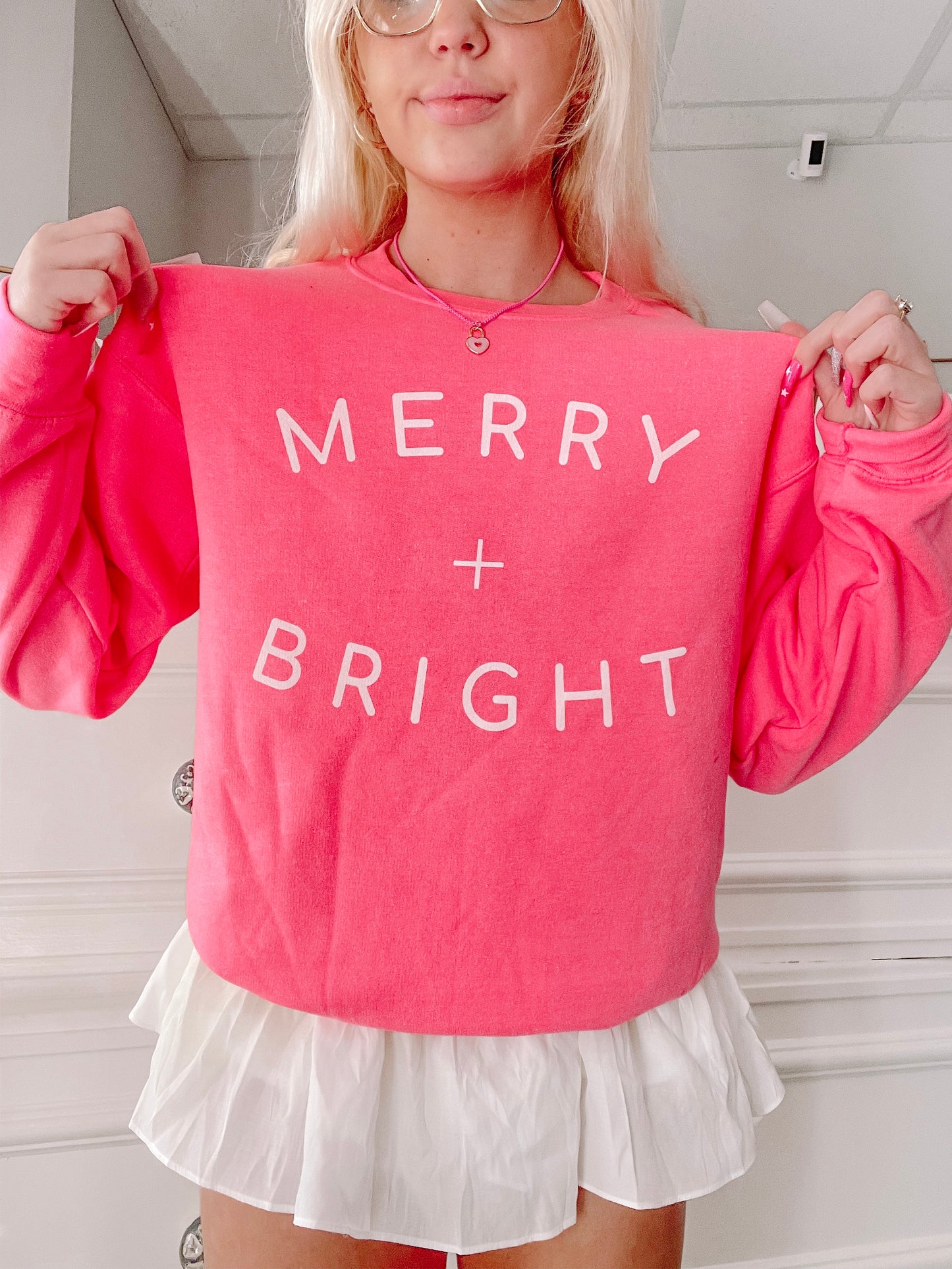 Bright pink crewneck sweatshirt with "Merry + Bright" in white lettering.