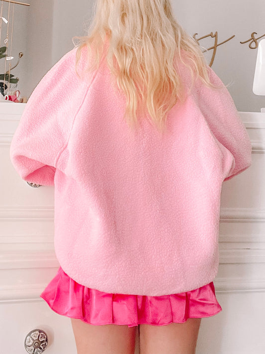 Bubblegum pink fleece jacket, shown from the back, paired with a hot pink pleated mini skirt.