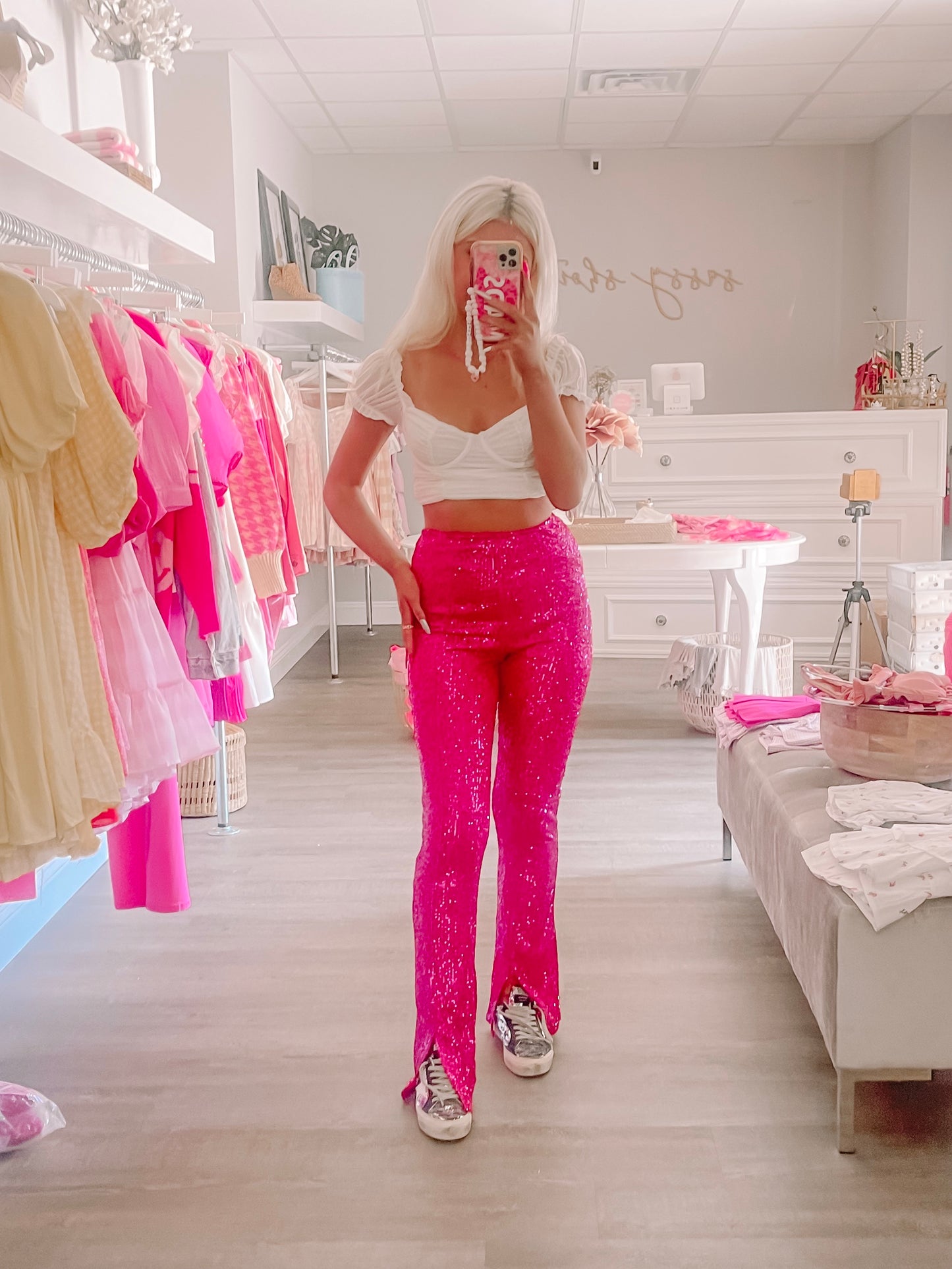 Hot pink sequined pants styled in a boutique; flared leg, worn with a white crop top.