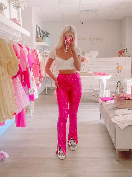 Hot pink sequined pants styled in a boutique; flared leg, worn with a white crop top.