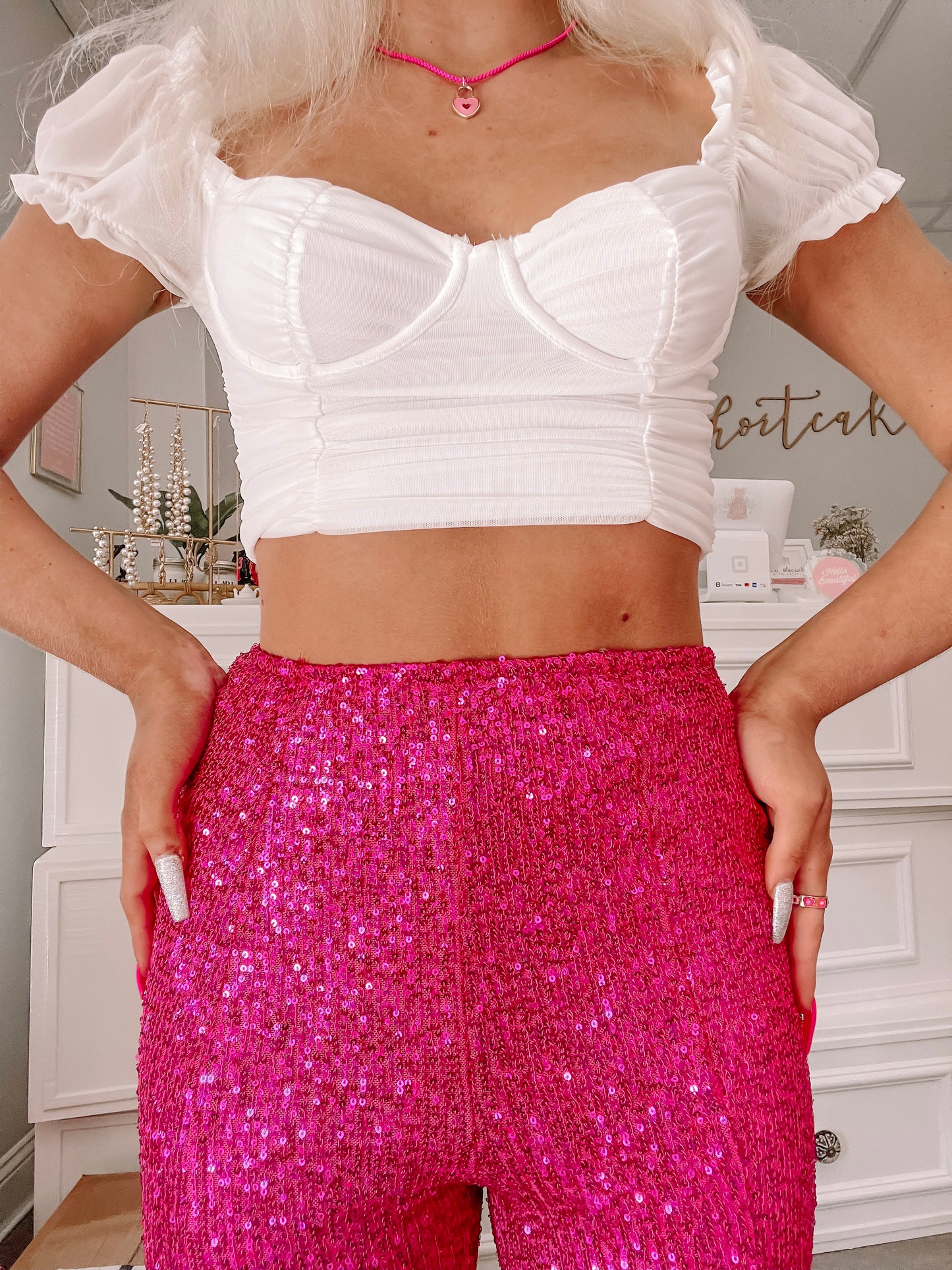 Hot pink sequined pants styled with a white crop top, shown on a model in a bright room.