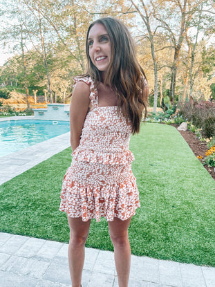 Woman in a peach floral smocked mini dress and ruffled skirt, near a swimming pool.