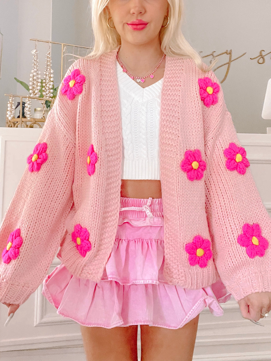 Pink knitted cardigan adorned with bright pink flowers, modeled with a pink skirt.