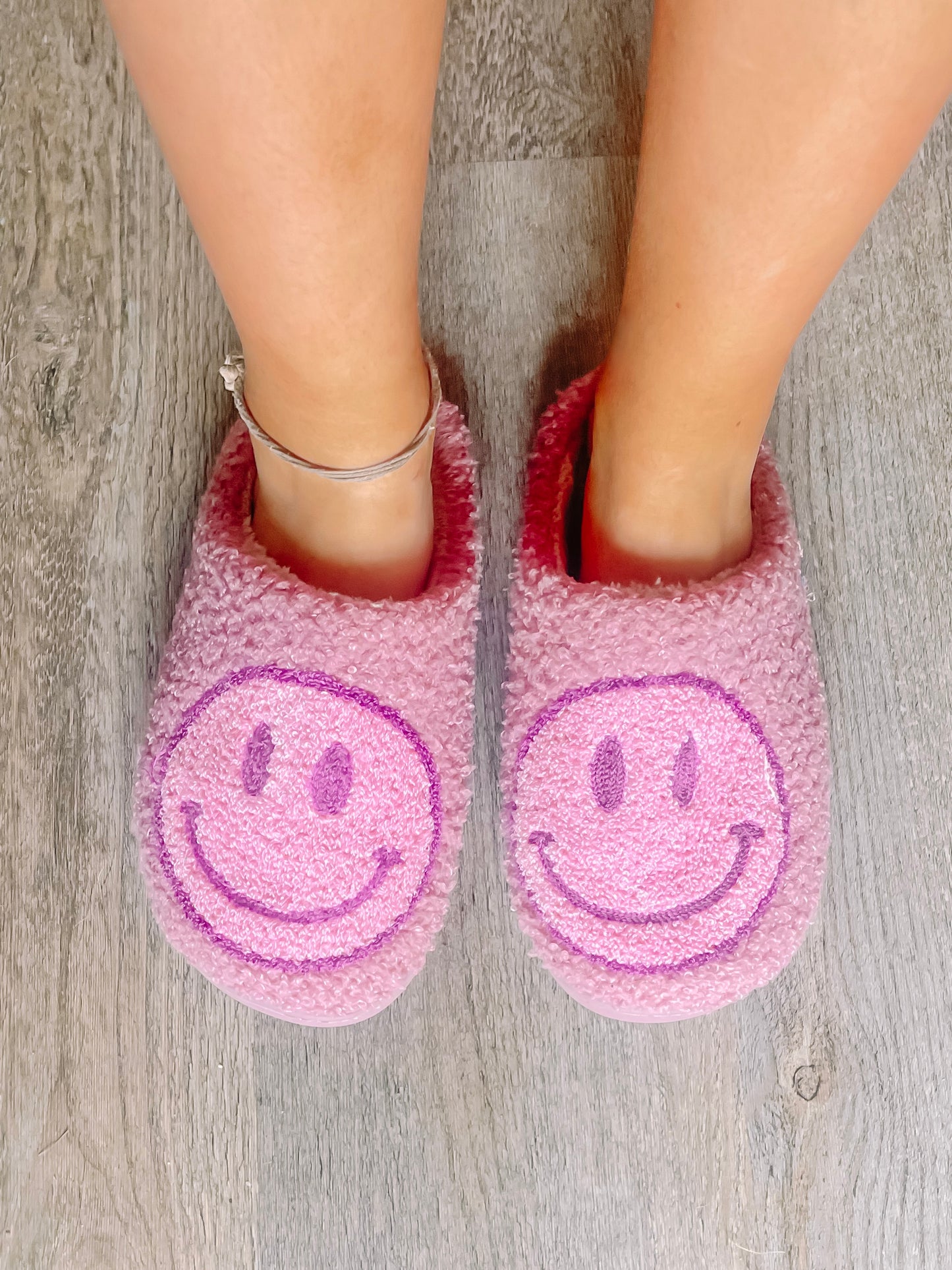 Pink fuzzy Sassy Slumber slippers with purple smiley faces, perfect for cozy nights.