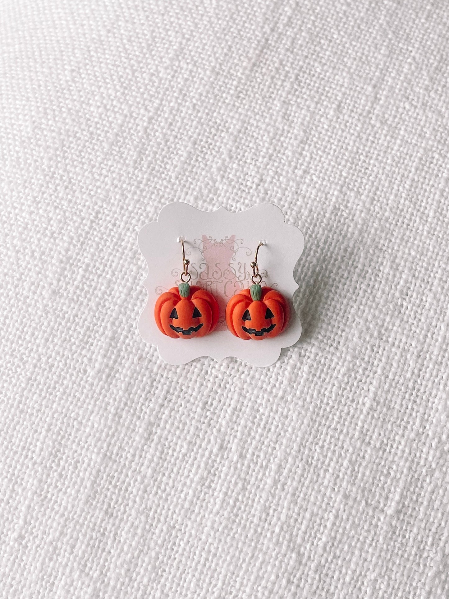 Cute jack-o'-lantern dangle earrings displayed on a textured white background.