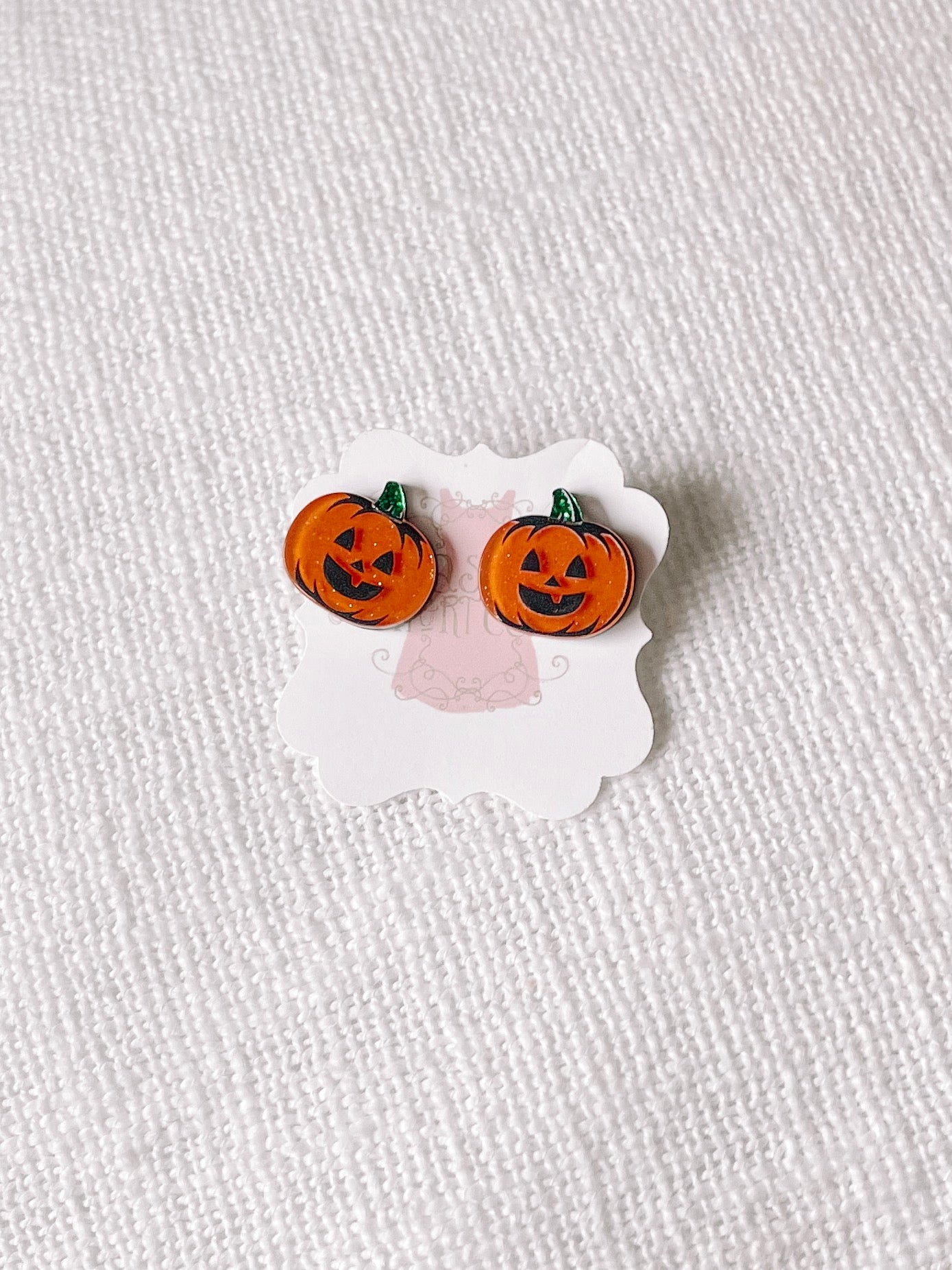 Jack-o'-lantern stud earrings displayed on a card against a textured white background.