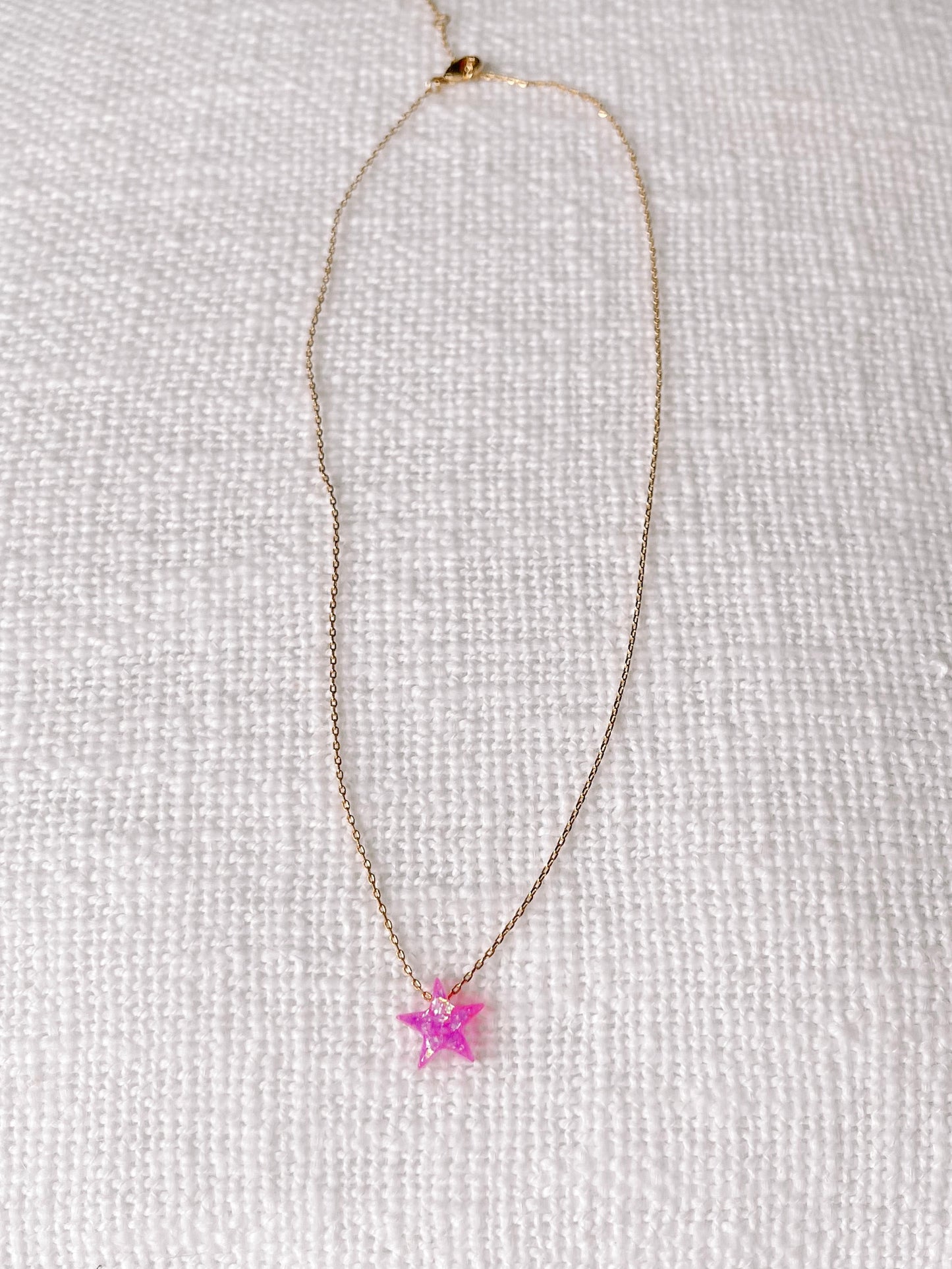 Pink opal star pendant on delicate gold chain, displayed on white textured fabric.
