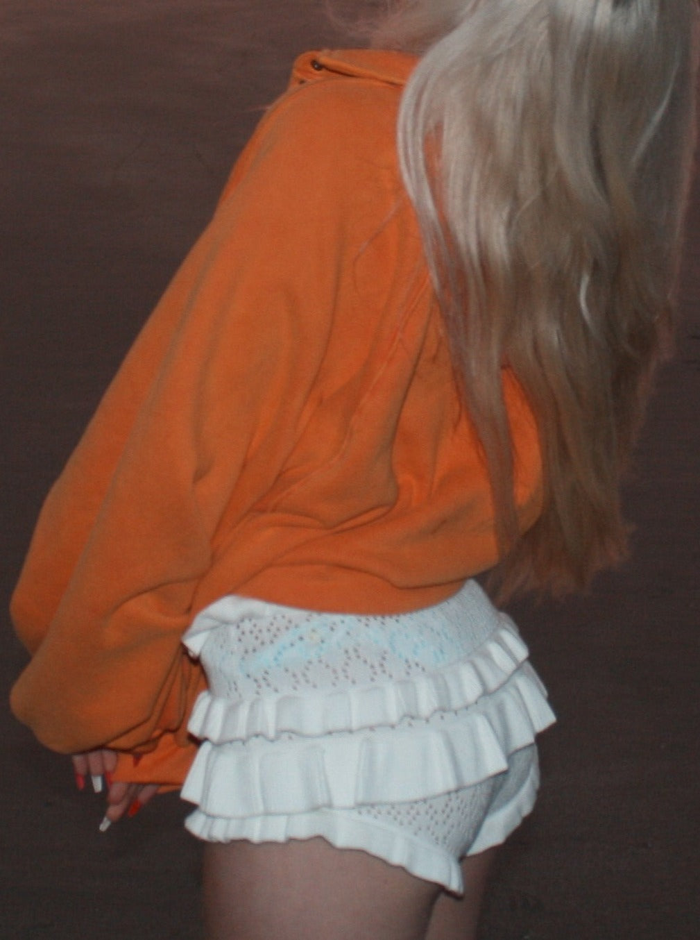 White ruffled knit shorts worn over a light blue underlayer, paired with an orange sweater.
