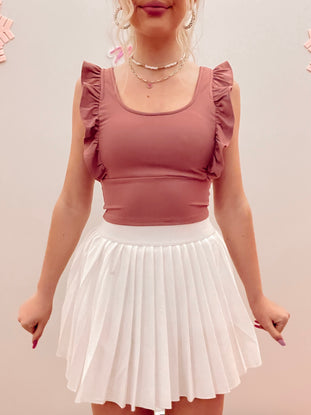 Dusty rose ruffle-trimmed crop top paired with a white pleated mini skirt.