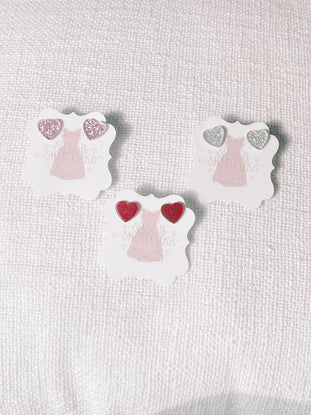 Glittery heart-shaped earrings displayed on individual cards, pink, silver, and red.