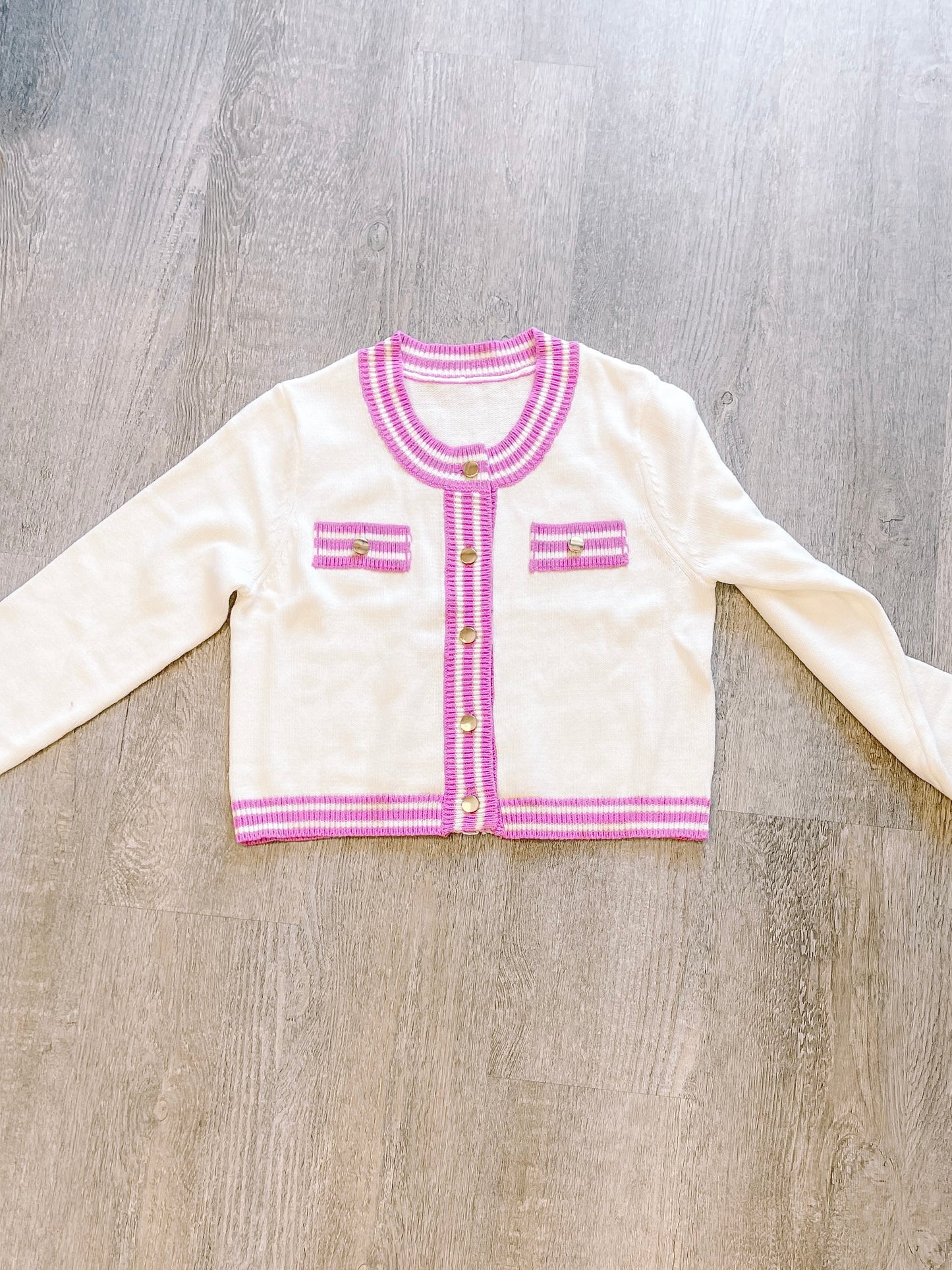 Cream-colored knit cardigan with purple trim, gold buttons, and flat lay presentation.