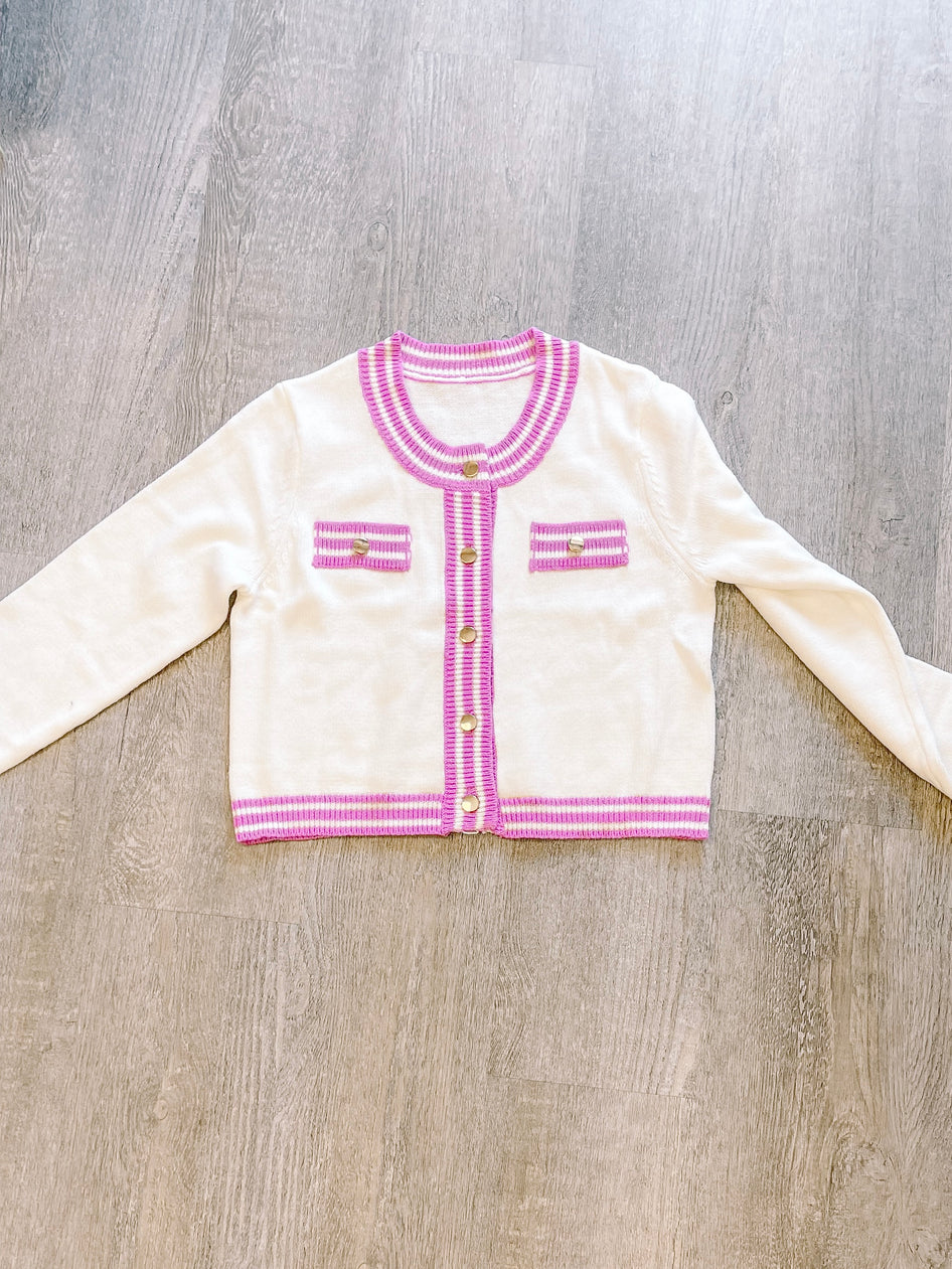Cream-colored knit cardigan with purple trim, gold buttons, and flat lay presentation.