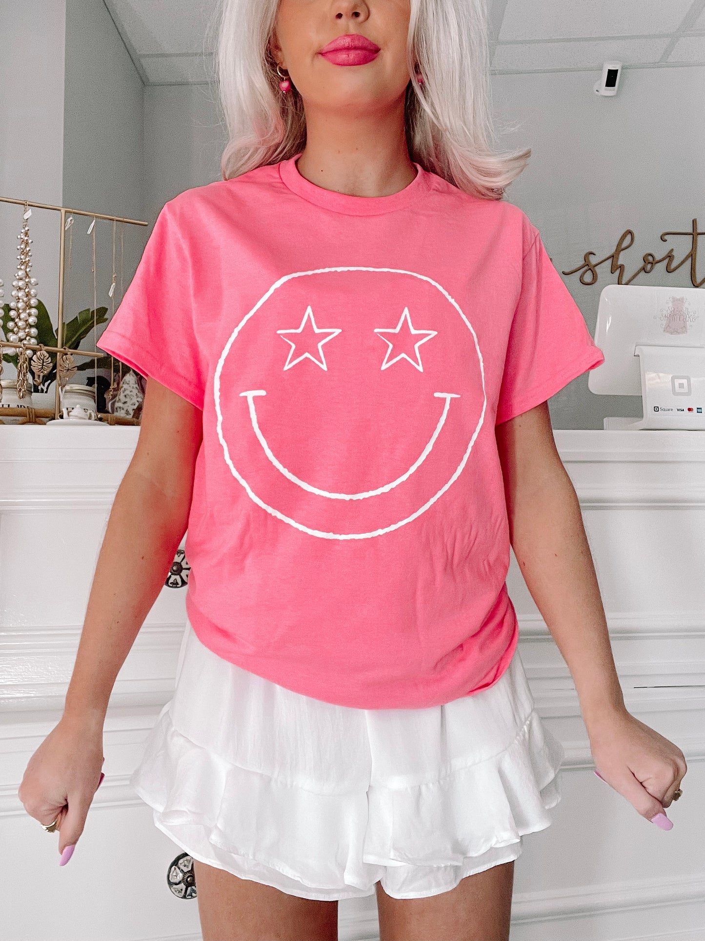 Pink Star Eyed Smiley Tee; playful graphic tee featuring a white smiley face with star eyes.