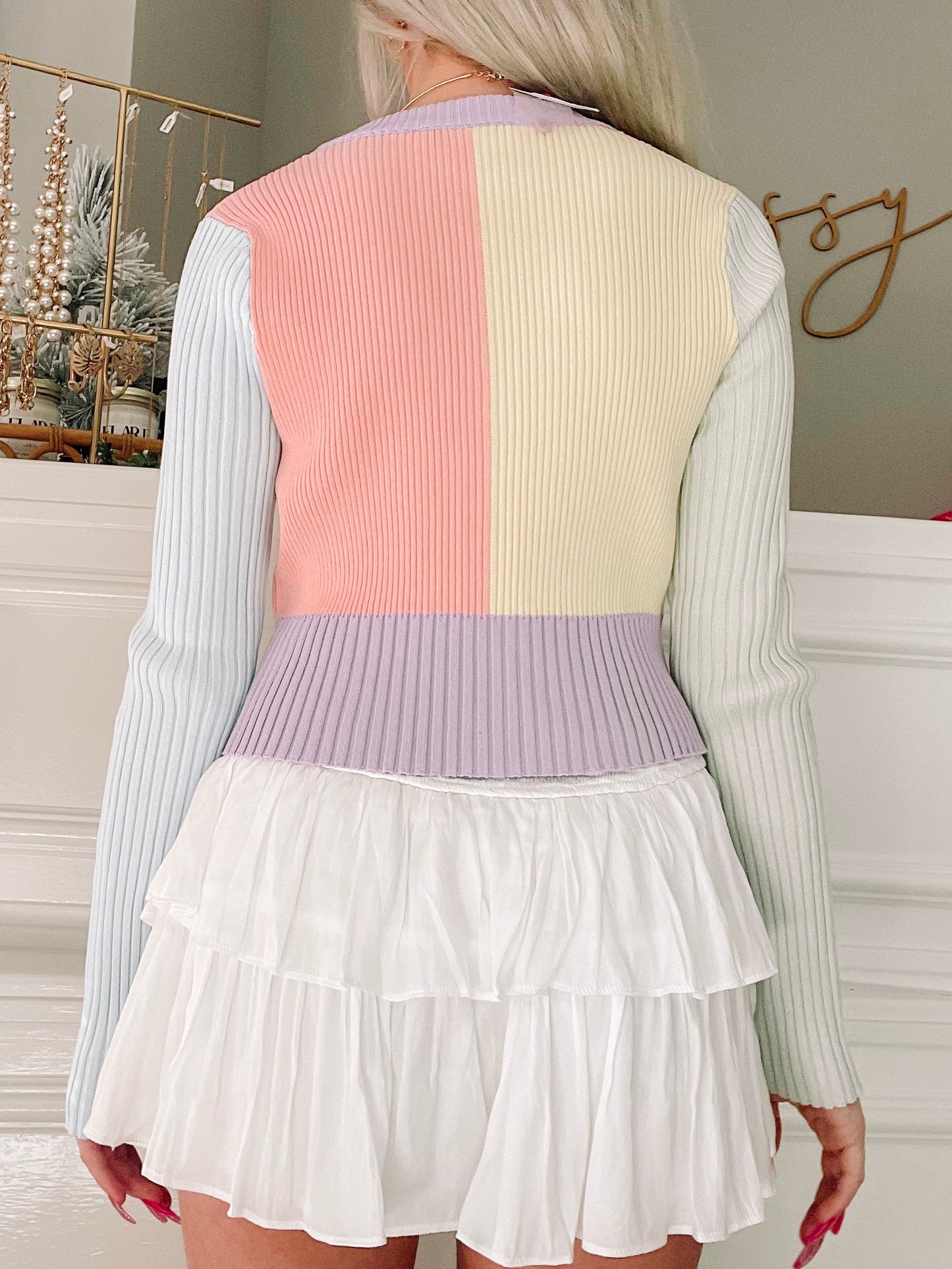 Pastel ribbed knit cardigan in peach, cream, and lavender, shown from the back with a white tiered skirt.