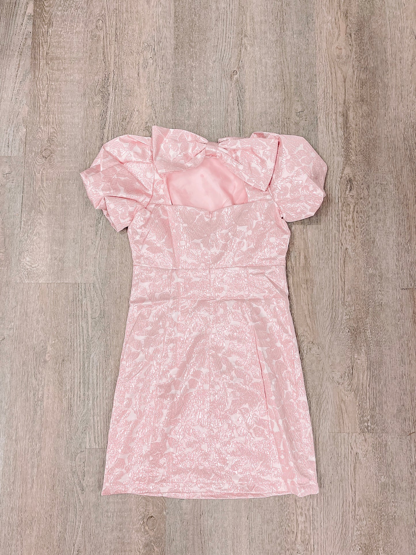 Pink patterned mini dress with puff sleeves and bow detail, laid flat on wood.