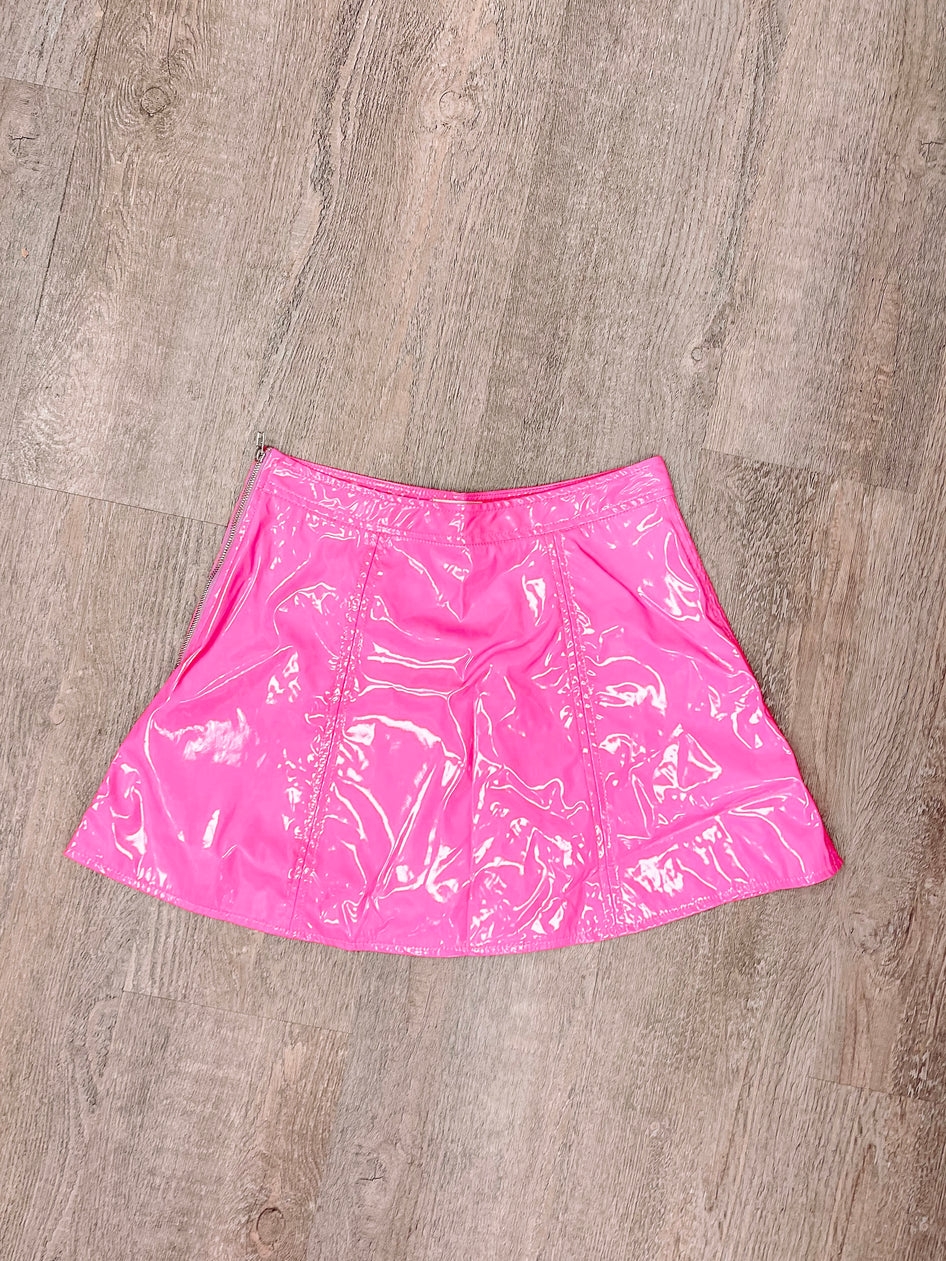 Shiny pink mini skirt with zipper detail, shown on wood background.