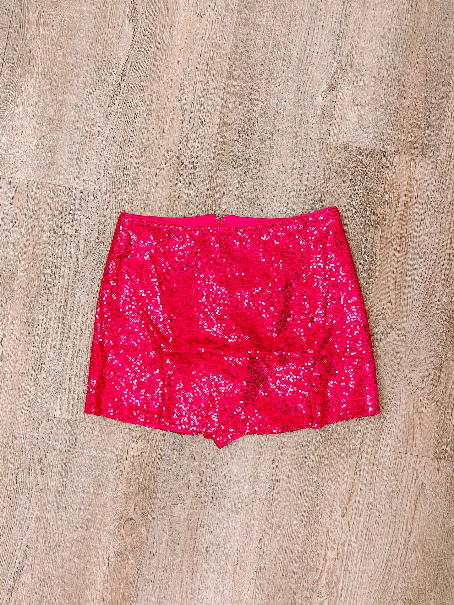 Hot pink sequined mini skirt laid flat on wood.