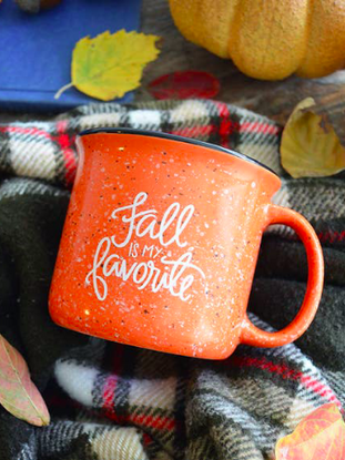 Speckled orange mug with "Fall is my favorite" in white script, nestled in a cozy plaid blanket.