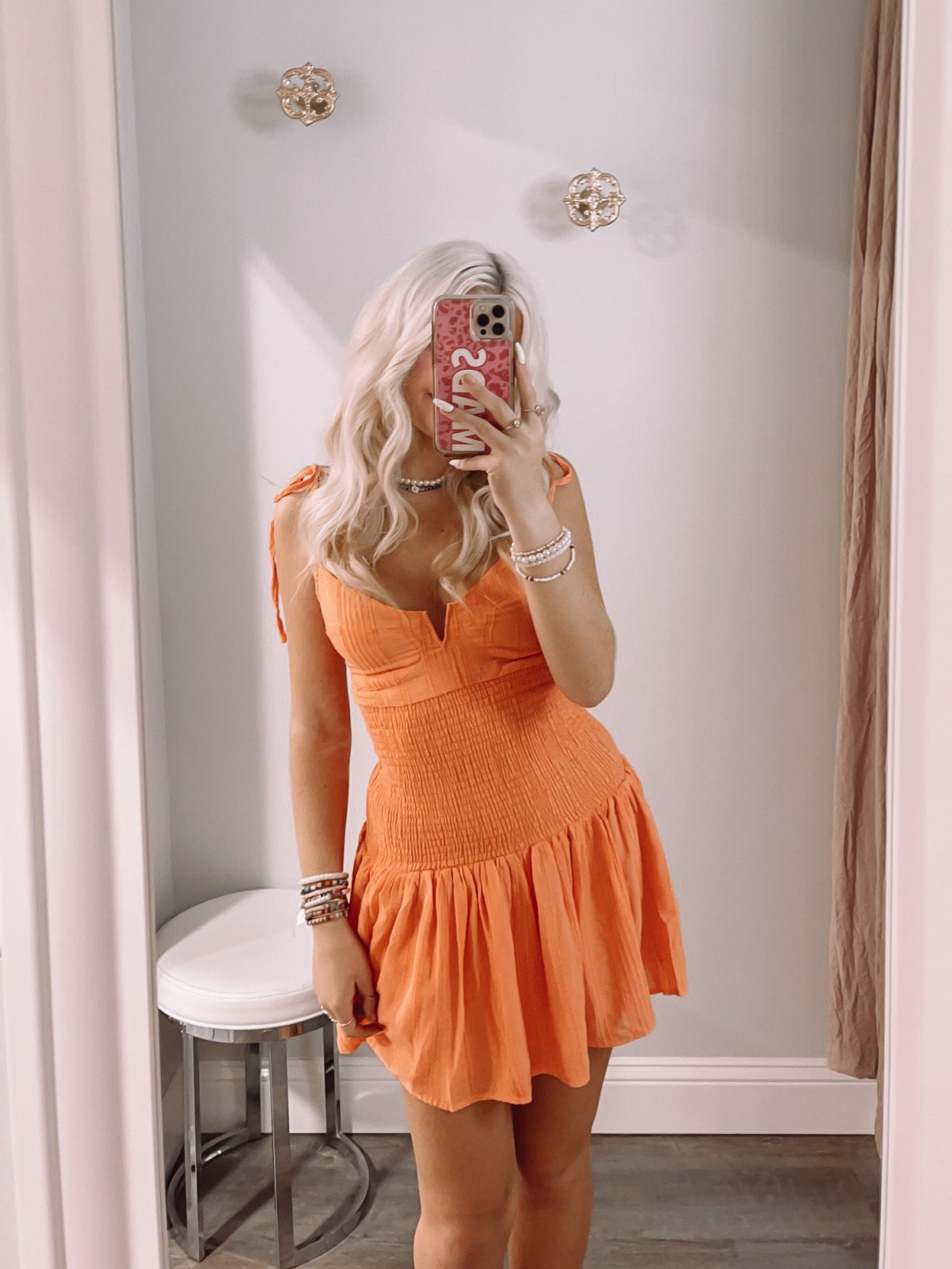Orange smocked mini dress with thin straps, modeled in a dressing room.