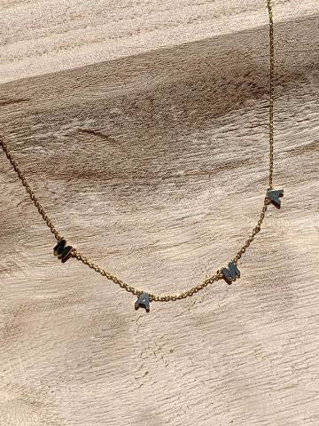 Gold chain necklace with dark gray "MAMA" lettering on light wood background