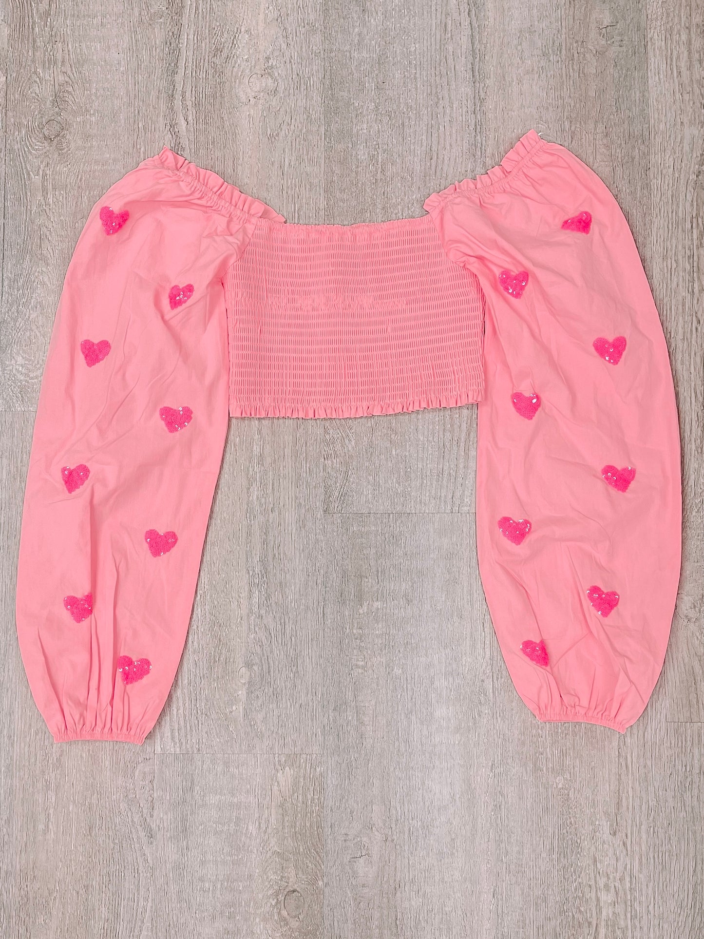 Pink off-the-shoulder top with embellished hearts, long sleeves, and smocked bodice.
