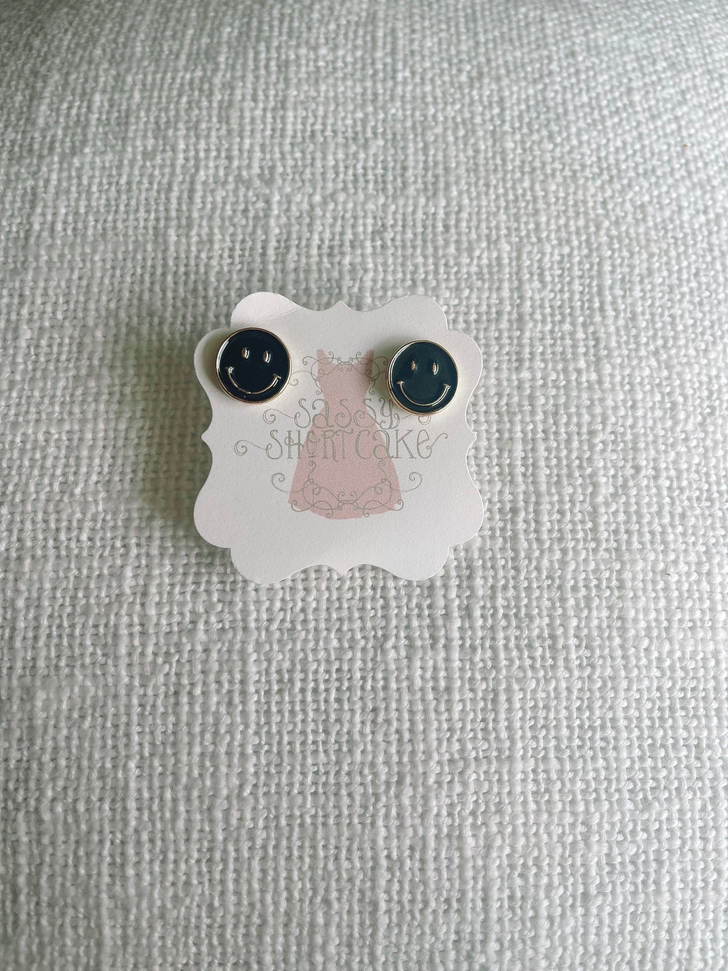Black smiley face stud earrings displayed on a white textured background.