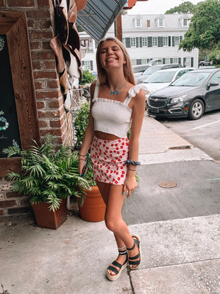 Woman in a white crop top and floral mini skirt, smiling outdoors.