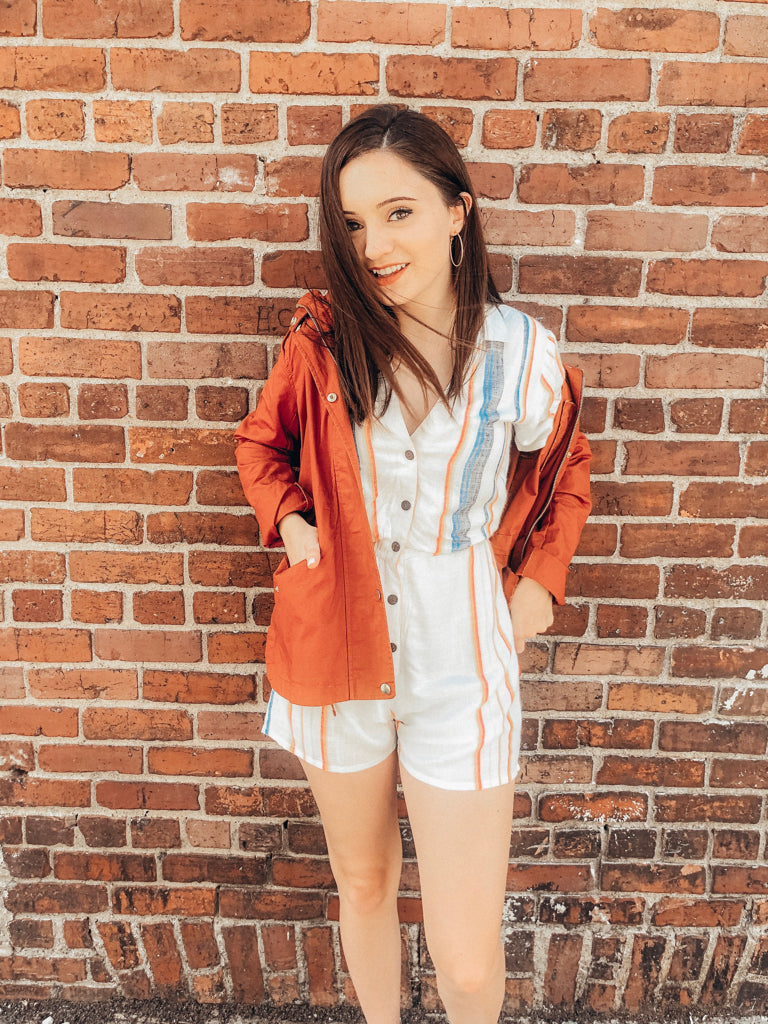 Woman in burnt orange jacket against brick wall
