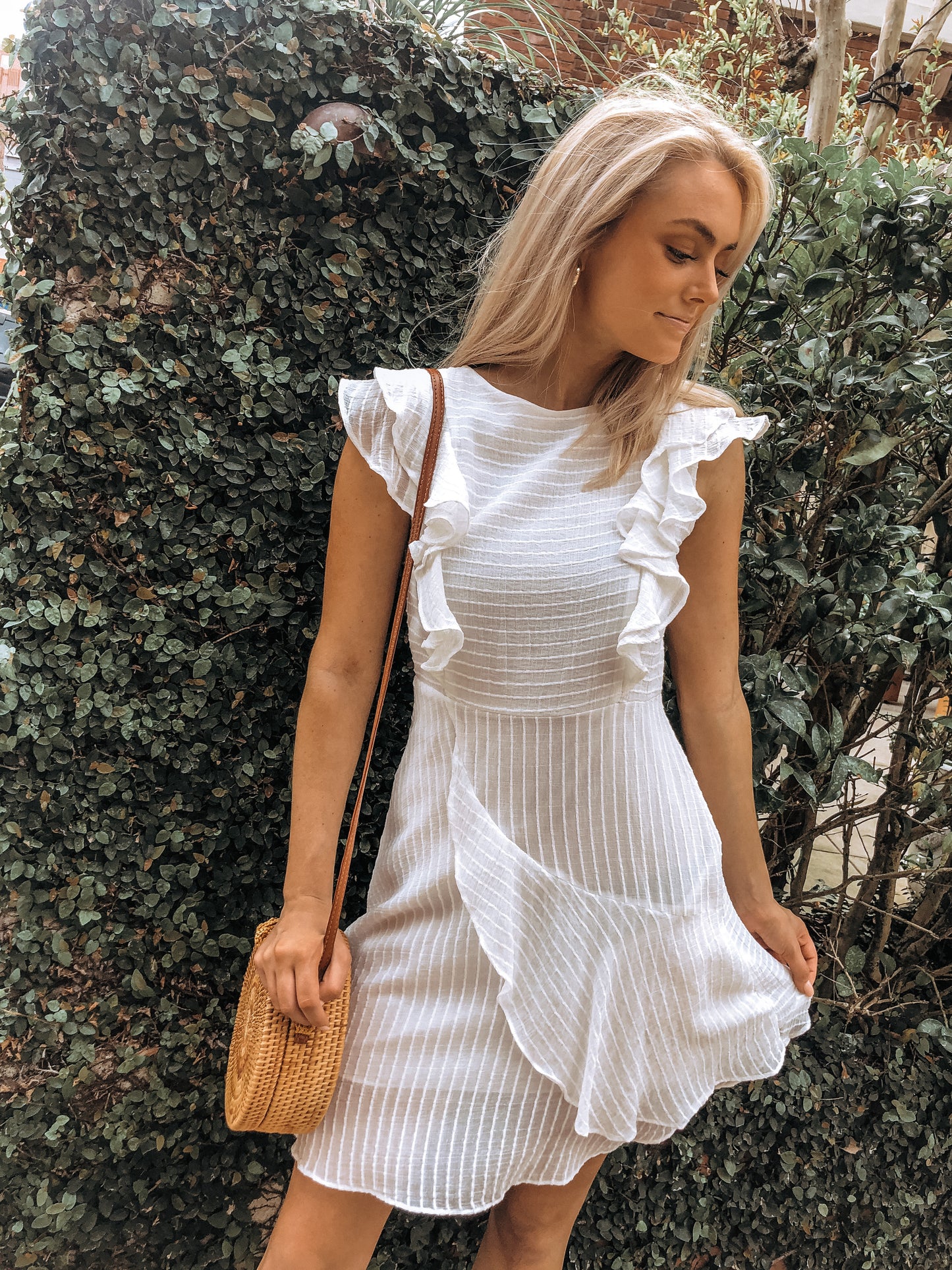 White eyelet mini dress with ruffled sleeves, styled outdoors against lush greenery.
