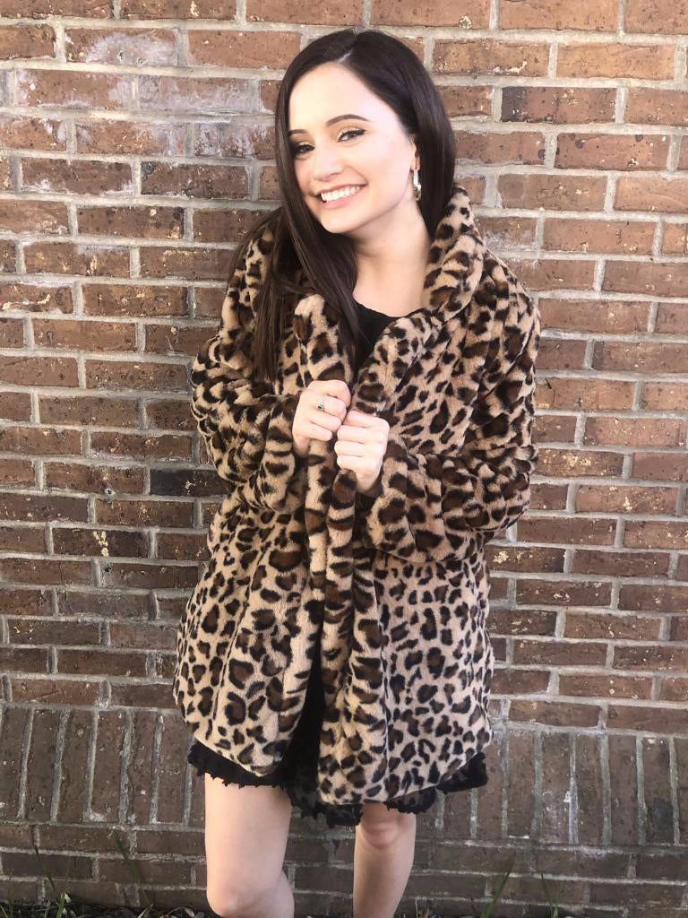 Leopard print faux fur coat, open front, modeled against a brick wall.