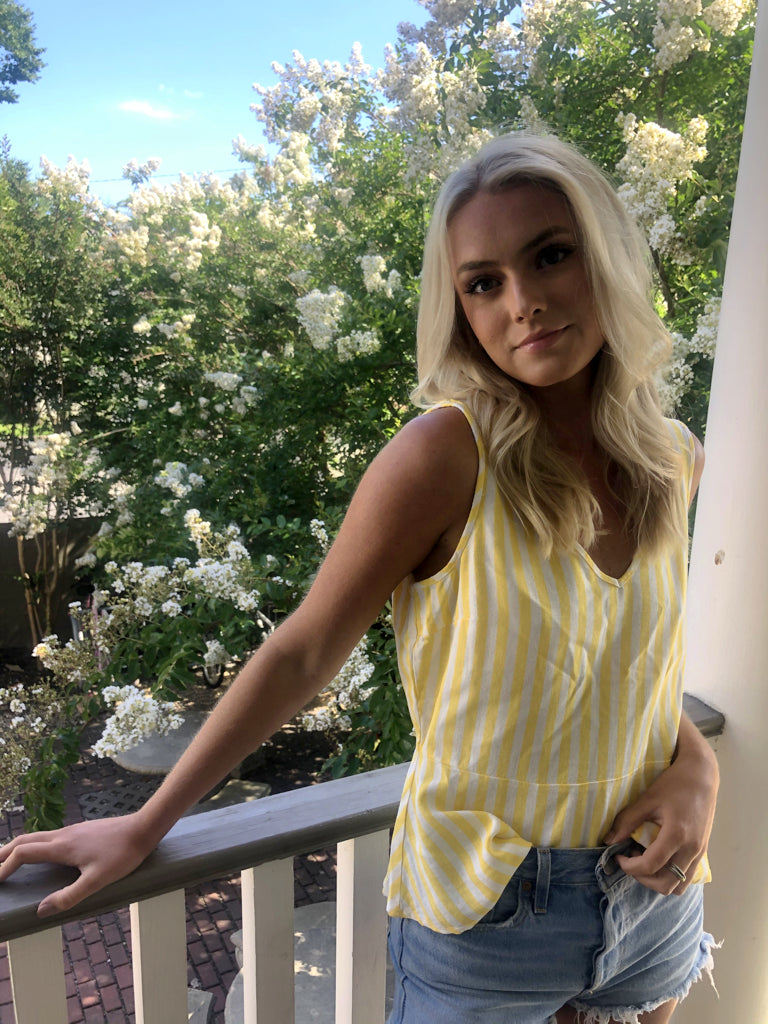 Woman in yellow and white striped tank top on porch, blooming trees in background