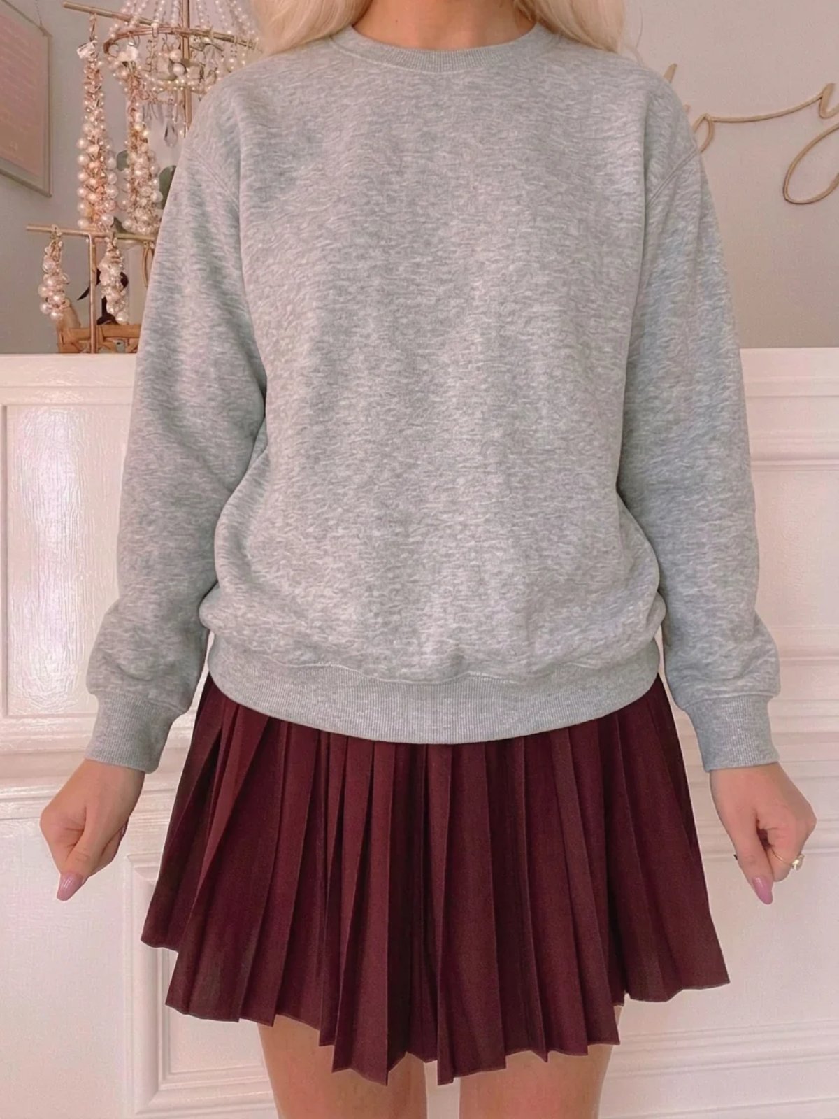 Burgundy pleated mini skirt paired with a white ribbed top featuring sheer, ruffled sleeves.