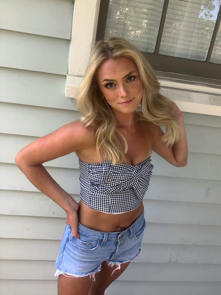 Woman in navy gingham crop top and denim shorts, posing outdoors.