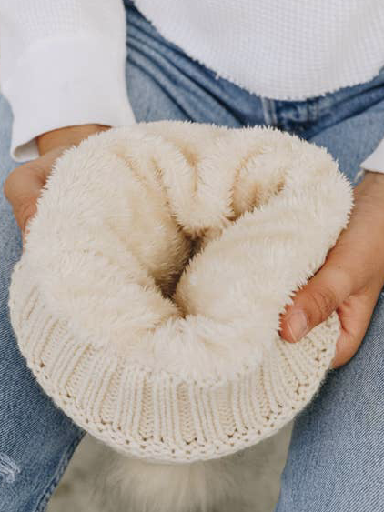 Cream-colored knit beanie with a fluffy fleece lining, shown being held.