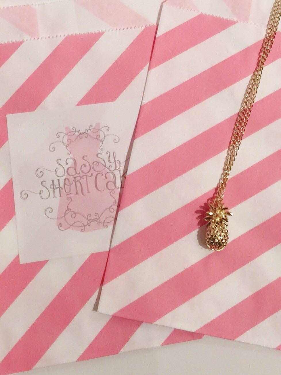 Gold pineapple necklace on pink striped bag
