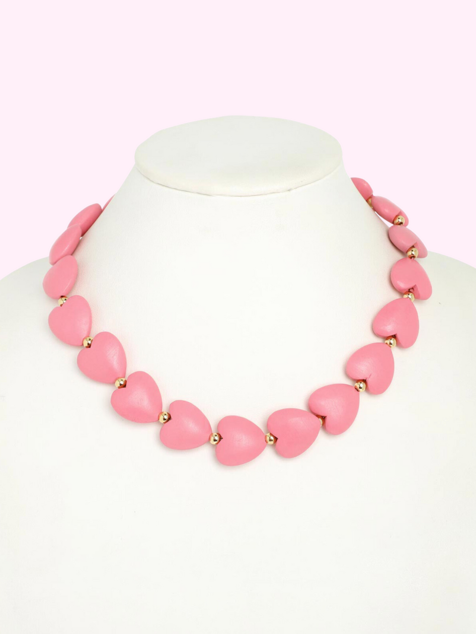 Pink heart necklace on a white mannequin, gold accents.
