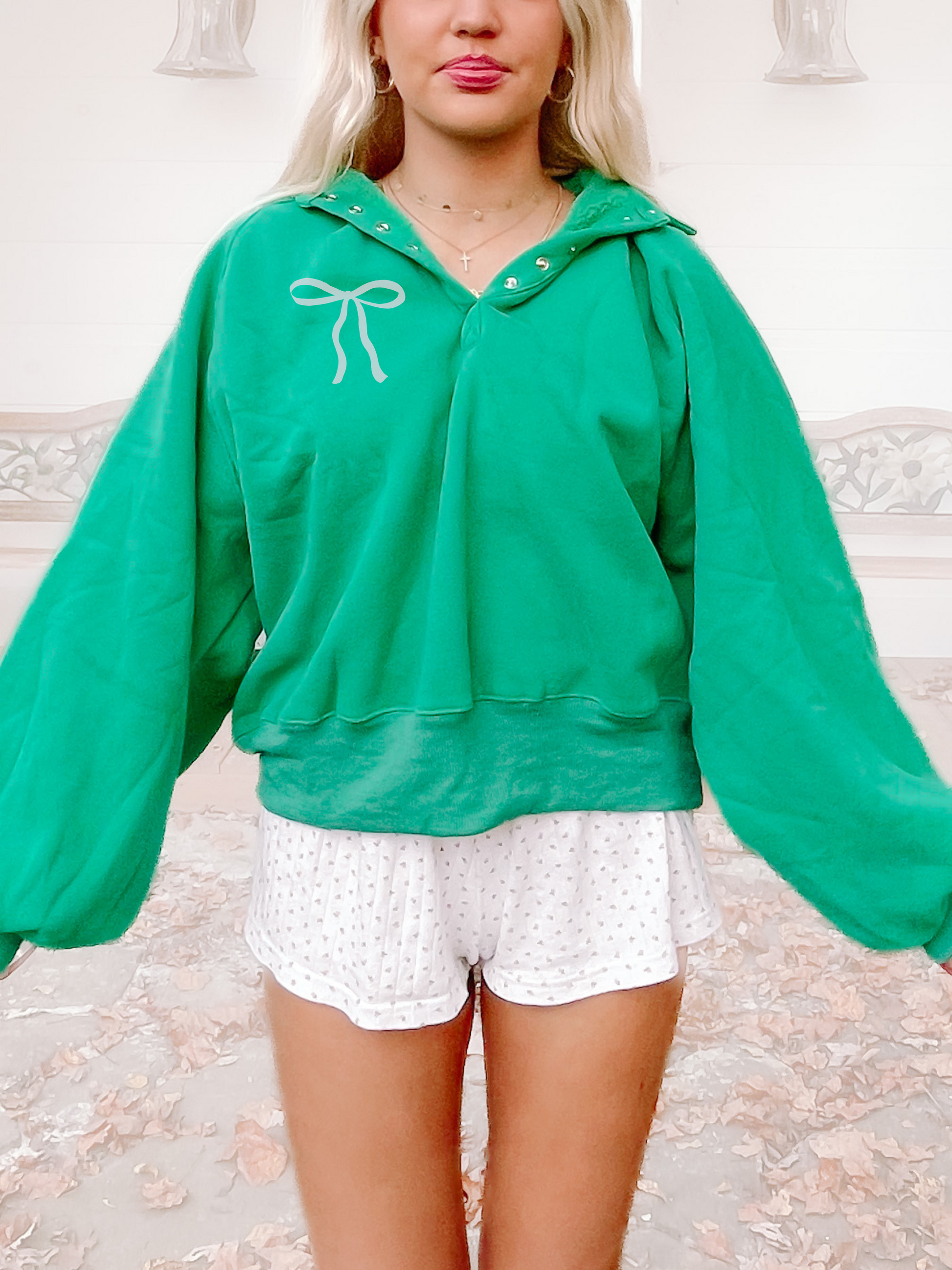 Bright green pullover sweatshirt with a subtle bow detail, shown on a model.
