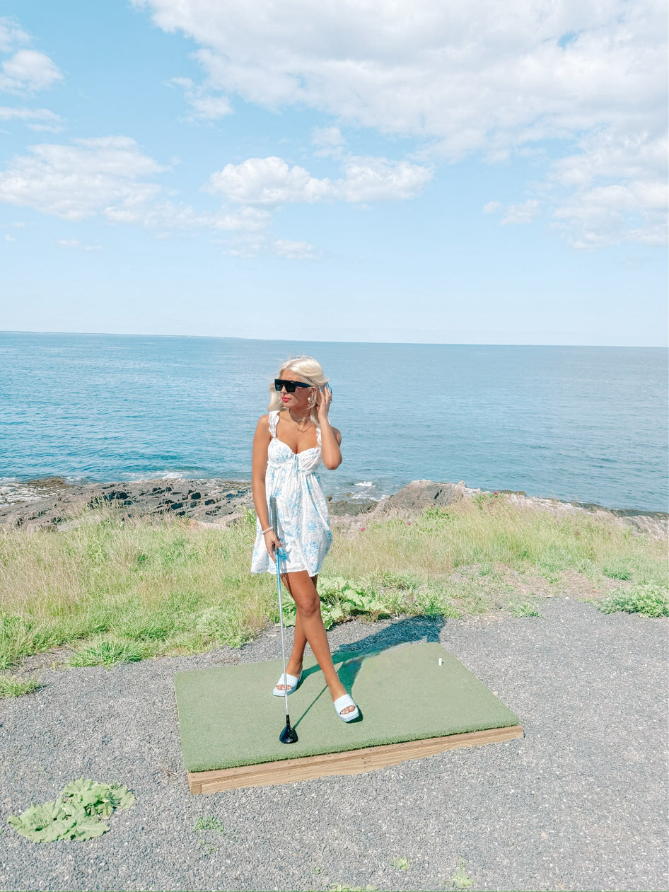 Woman in floral dress golfing by the ocean.
