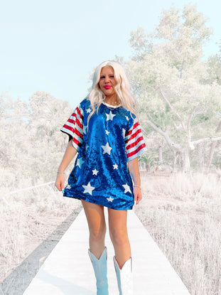 Sequin mini dress with stars and stripes sleeves, modeled outdoors on a boardwalk.
