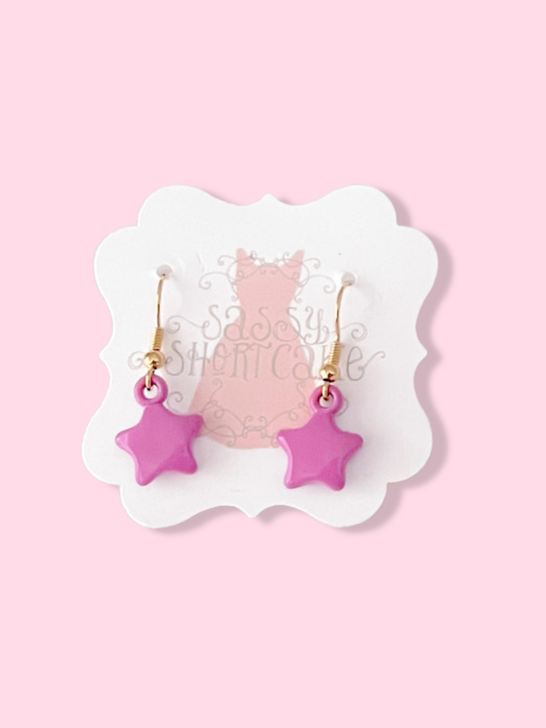 Pink star-shaped earrings on a display card against a pink background.
